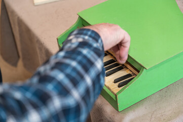 An elderly man plays a toy piano. His right hand presses the keys of an old children's instrument....