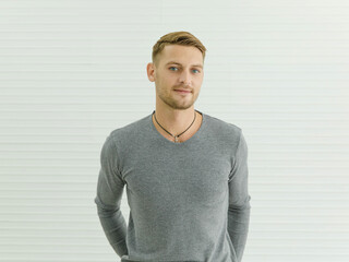 Portrait studio shot of Caucasian young smart cool handsome blonde hair blue eyes male fashion model in gray long sleeve shirt standing crossed arms look at camera on white stripe wall background