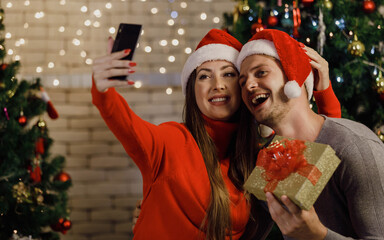 Caucasian lover couple husband giving Xmas present gift box to wife in sweater and red Santa Claus...