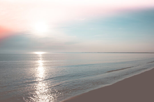 Beach with calm ocean under beautiful pastel sunrise.