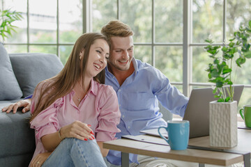 Millennial happy young lover couple husband and wife sitting cuddling on floor in living room drinking coffee watching comedy streaming online movie via laptop notebook computer together on weekend