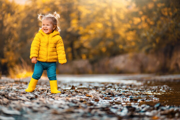 A smiling child girl in yellow rubber boots is playing on the river bank. Copy space. Concept of...