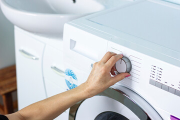 adult woman turns on washing machine in bright bathroom