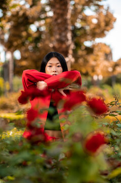 Retrato artístico de una elegante mujer asiática vestida con un traje rojo en un jardín con flores rojas