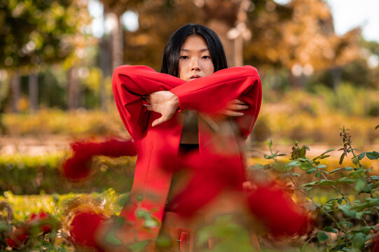 Retrato artístico de una elegante mujer asiática vestida con un traje rojo en un jardín con flores rojas