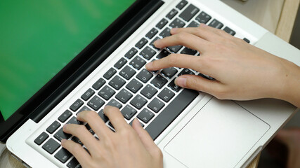 Close up of woman's hands typing on laptop with green screen, using laptop for working.