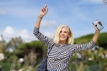 Mature woman strolling along a seaside spot near the beach, raising her arms in joy.
