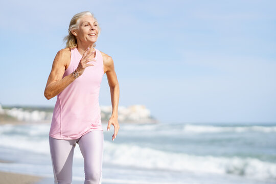 Mature woman running along the shore of the beach. Older female doing sport to keep fit