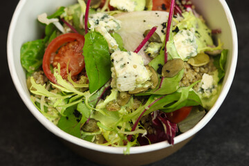 Healthy salad with beetroot, blue cheese, tomatoes, quinoa and 
pumpkin seeds in eco paper package for take away or food delivery isolated on black background. Top view. Keto diet.