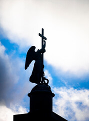 Dark silhouette of an angel with cross striking serpent on the Pillar of Alexandria against the sky.