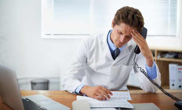 There Has To Be Another Treatment. Shot Of A Concerned Doctor Sitting In His Office And Talking On The Phone While Looking Over Paperwork.