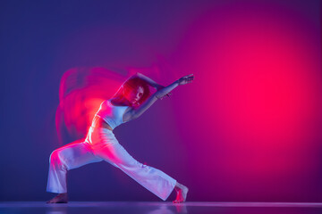 Young sportive beautiful girl, hip-hop dancer dancing hip hop isolated on purple background in pink neon light. Youth culture, style and fashion, action.