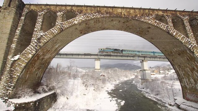 Train goes over the modern metal bridge with an old stone viaduct in foreground at winter Vorokhta, Ukraine