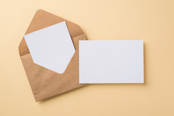 Top view of big brown craft envelope with two white postcards situated on beige isolated background blank space