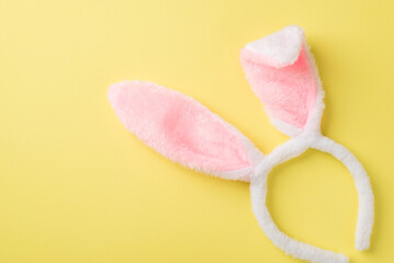 Top view photo of the white and pink soft cute headband in shape of rabbits ears on the isolated yellow background blank space
