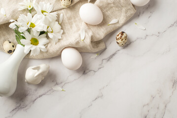 Top view photo of the white vase with daisies few eggs and ceramic rabbit on the textured cloth on isolated marble empty background