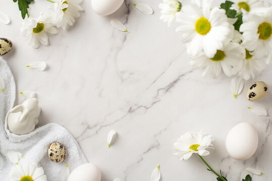 Top view photo of easter decorations bouquet of chrysanthemum flowers petals ceramic easter bunny statuette cloth and eggs on isolated white marble texture background with empty space in the middle