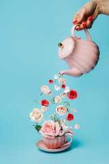 Creative layout with hand holding teapot and pouring fresh flowers and leaves into tea cup on...