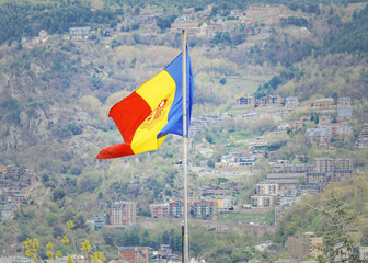 Flag of Andorra on the background of mountains and houses. - obrazy, fototapety, plakaty
