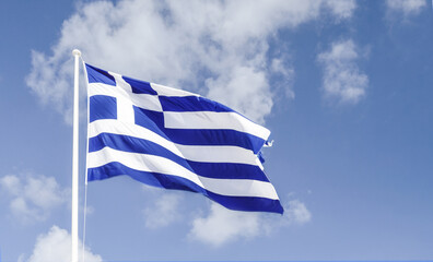 The Greek flag flying in the wind against the blue sky.