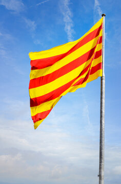 Flag of Catalonia against a blue sky with clouds.