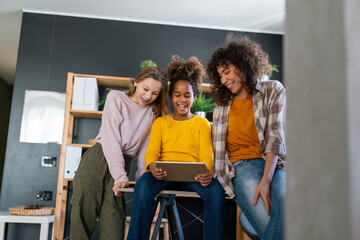 Happy multiethnic teenagers holding technology gadgets using digital devices studying together.