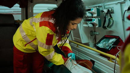Young Ethnic Female Paramedic Helping Out a Patient In the Ambulance Car, Inserting an IV Drip Into...