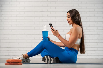 Guapa mujer deportista sujetando el teléfono móvil con una mano y con la otra un bidón de bebida