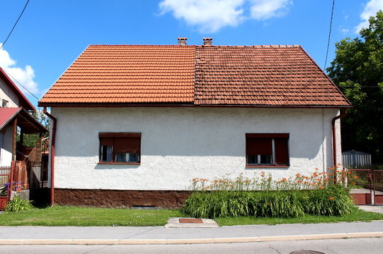 Attached Small Suburban Family House With Two Owners Split In The Middle With Left Half Covered With New Red Roof Tiles And Right One With Dilapidated Old Roof Tiles Built Next To Paved Public