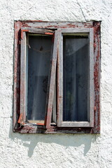 Fototapeta na wymiar Broken destroyed window with double glass inside dilapidated wooden frame held together with metal support on side of abandoned suburban family house surrounded with cracked white facade on warm sunny