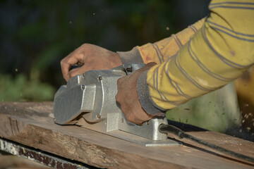 Man using electric scraper to plane wooden plank. Blur background.