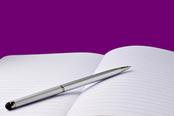 Silver ballpoint pen on notebook, violet background.