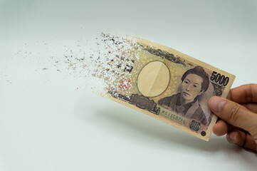 The man's hand holds a 5,000 yen, which crushes and flutters in the wind. The concept of currency...