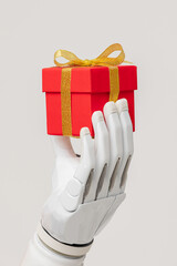 a bionic prosthetic arm or forearm in white on a beige background holds a red gift, prosthetics of...