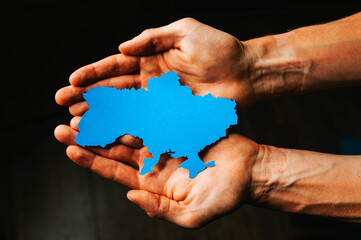 Support for Ukraine in the war with Russia. Hands holding the flag of Ukraine in the shape of the borders of Ukraine.