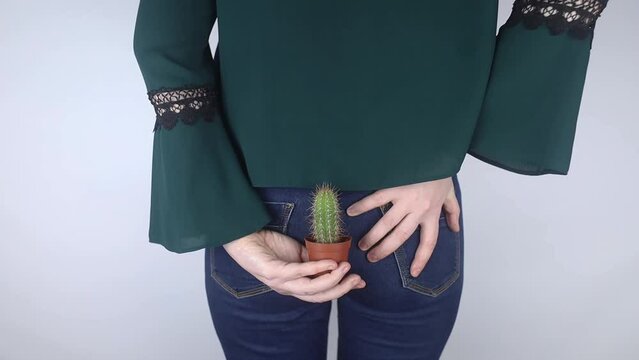 Concept. A woman holds a cactus as a symbol of rectal pain. Varicose veins of the lower intestine. Pain in the rectum, hemorrhoids and pain in the excretory system of the body. Proctology