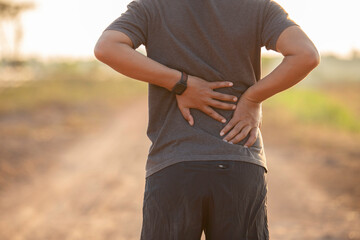 Asian man walking for exercise and has back pain in the park in the morning and evening.