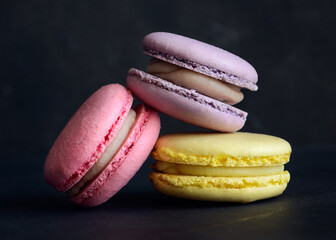 Stack of three macarons on dark background. Delicious pink, purple and yellow macaroons. Horizontal photo. Macaron close-up. 