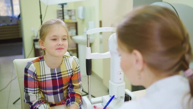 doctor interviews little girl before being examined in ophthalmologist's office.