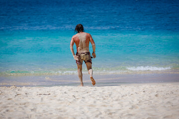 A man runs to swim in the blue sea. The back of the body is covered with sand