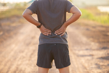 Asian man walking for exercise and has back pain in the park in the morning and evening.