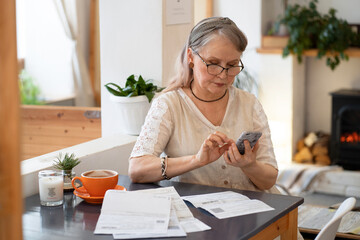 Elderly woman pays bills by phone - obrazy, fototapety, plakaty