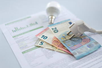 a white electric cap, a light bulb and euro banknotes on an electricity bill. Increase in the cost of electricity. Payment of electricity bills. Increasing the concept of electricity prices.