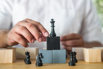 Businessman placing chess figure of king on top of stacked wooden blocks.