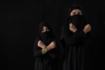 Muslim female wearing hijab or nigab crossed with her arms in an X, isolated on black background