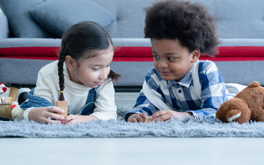 Cute little Caucasian and African kids girl and boy lying on floor smiling and playing toys build...