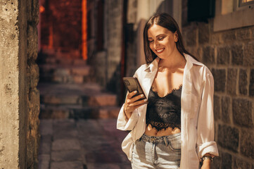 Beautiful young woman using smartphone while walking on the city streets on the coast during the sunset