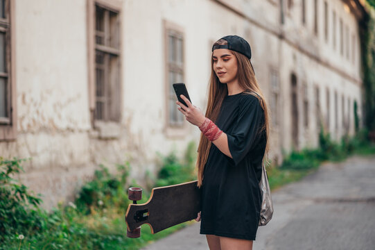 Young woman holding on her longobard and using a smartphone while walking on the road