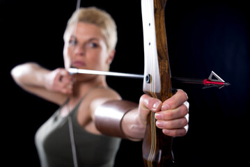 Young woman shooting with bow and arrow isolated on black background.