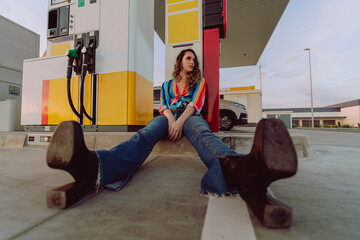 Chica joven delgada con pelo largo ondulado posando y tomándose fotos en una gasolinera